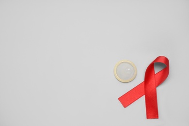 Red ribbon and condom on light grey background, flat lay with space for text. AIDS disease awareness Photo of Red ribbon and condom on light grey background, flat lay with space for text. AIDS disease awareness