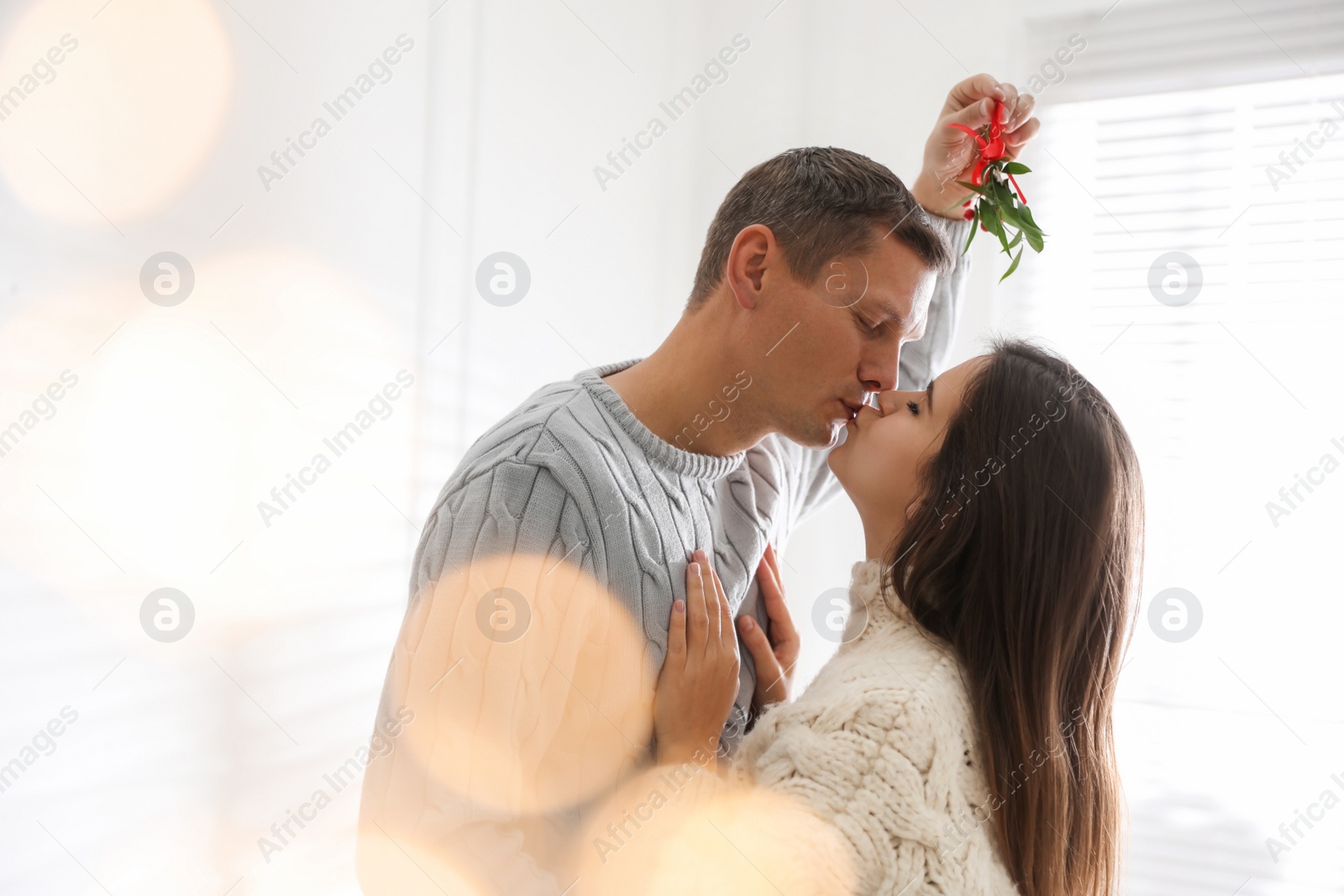 Happy couple kissing under mistletoe bunch at home, bokeh effect Photo of Happy couple kissing under mistletoe bunch at home, bokeh effect