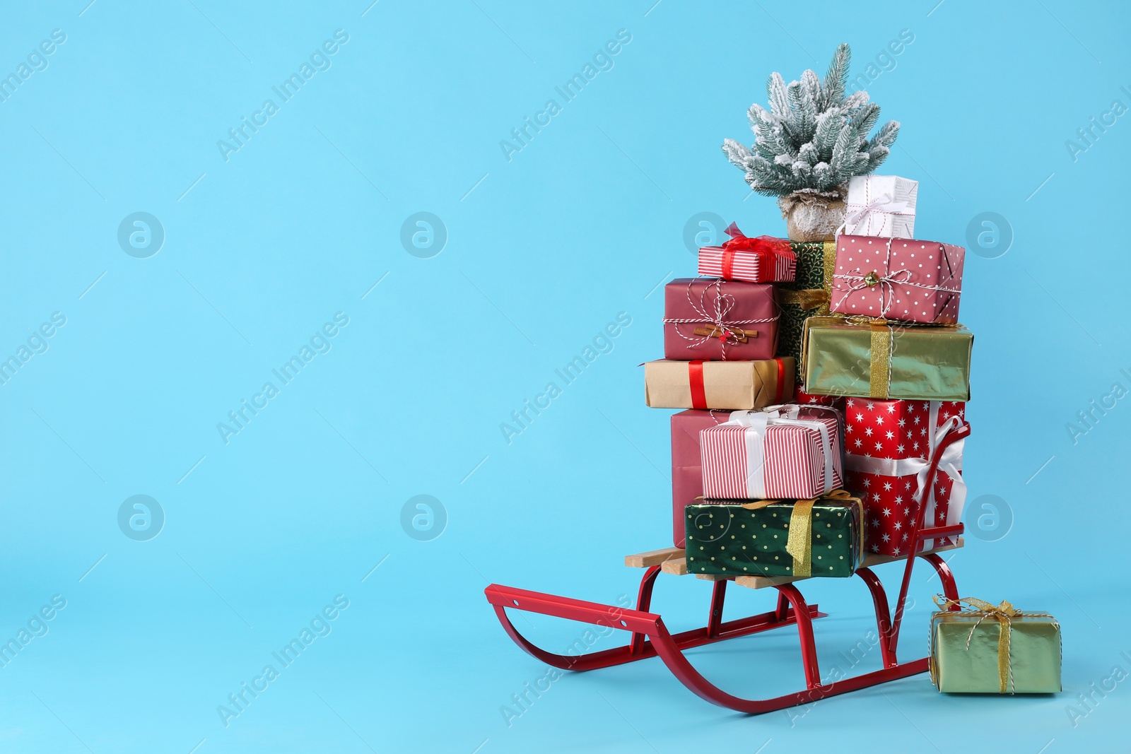Sleigh with gift boxes and small fir on light blue background. Space for text Photo of Sleigh with gift boxes and small fir on light blue background. Space for text