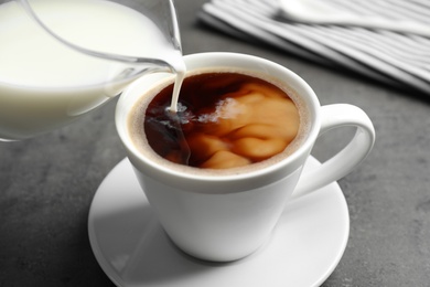 Pouring milk into cup of hot coffee on grey table, closeup Photo of Pouring milk into cup of hot coffee on grey table, closeup
