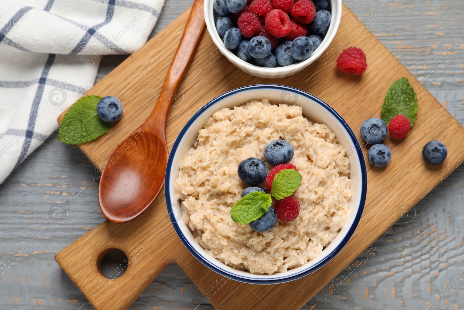 Tasty oatmeal porridge with berries on grey wooden table, flat lay Photo of Tasty oatmeal porridge with berries on grey wooden table, flat lay