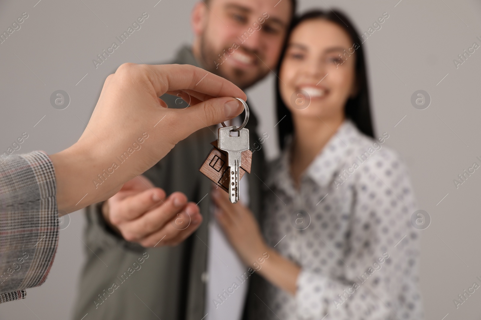 Real estate agent giving key to happy young couple against grey background, closeup Photo of Real estate agent giving key to happy young couple against grey background, closeup