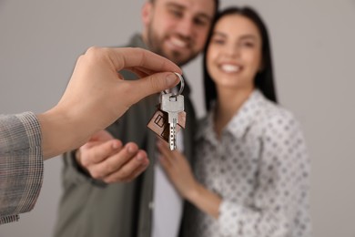 Real estate agent giving key to happy young couple against grey background, closeup Photo of Real estate agent giving key to happy young couple against grey background, closeup