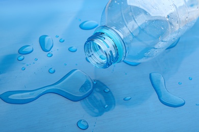 Drops of spilled water and plastic bottle on blue background, closeup Photo of Drops of spilled water and plastic bottle on blue background, closeup