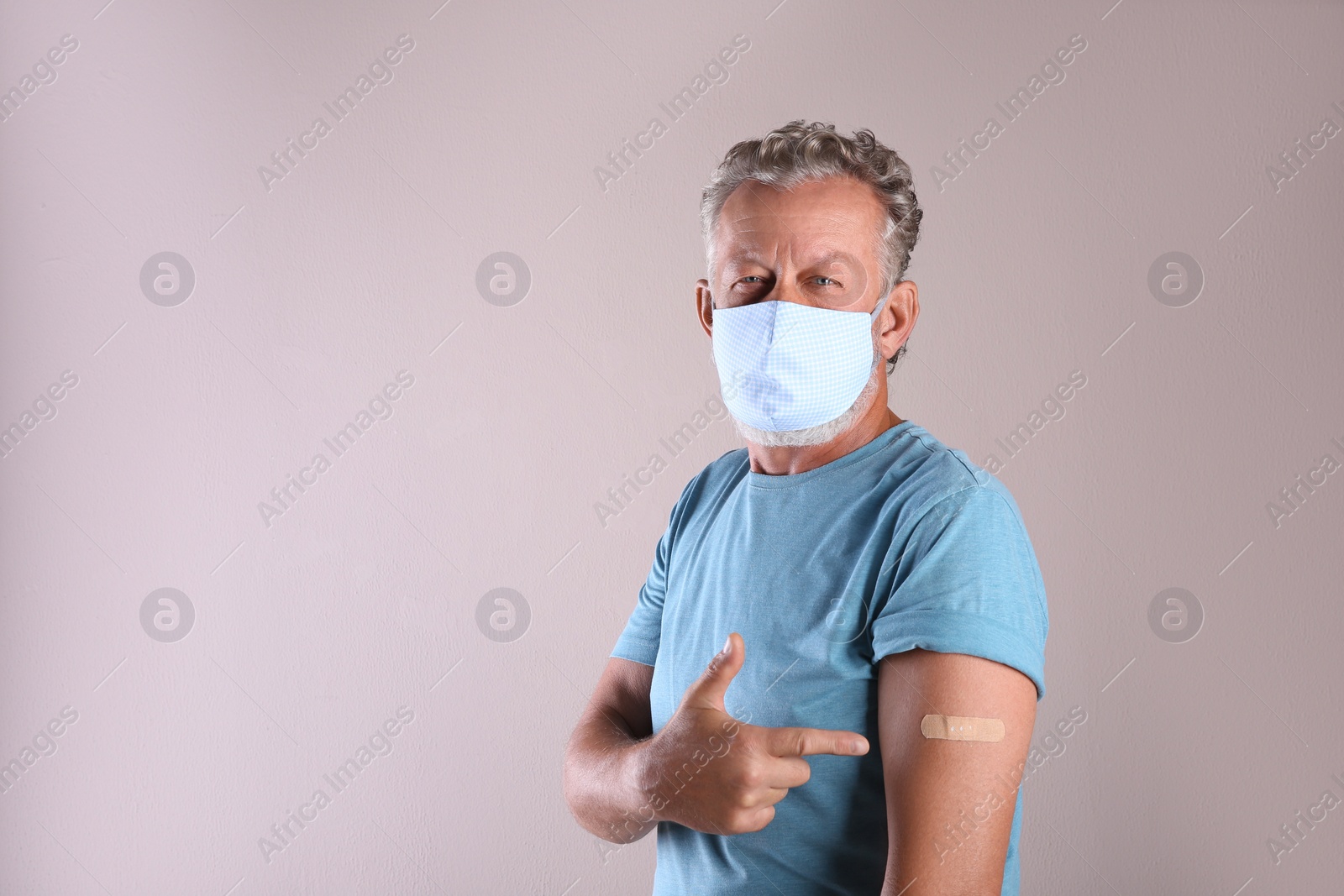 Senior man in protective mask pointing at arm with bandage after vaccination on beige background. Space for text Photo of Senior man in protective mask pointing at arm with bandage after vaccination on beige background. Space for text