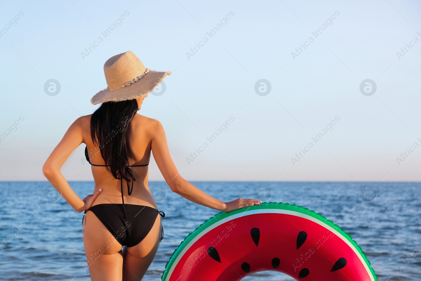Young woman in black stylish bikini with inflatable ring on beach, back view Photo of Young woman in black stylish bikini with inflatable ring on beach, back view