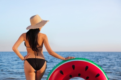 Young woman in black stylish bikini with inflatable ring on beach, back view Photo of Young woman in black stylish bikini with inflatable ring on beach, back view