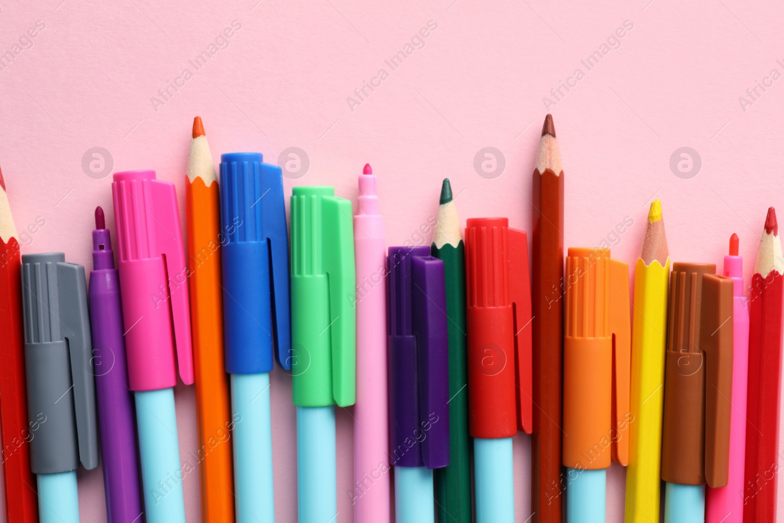 Different colorful pencils and felt tip pens on pink background, flat lay. Diversity concept Photo of Different colorful pencils and felt tip pens on pink background, flat lay. Diversity concept