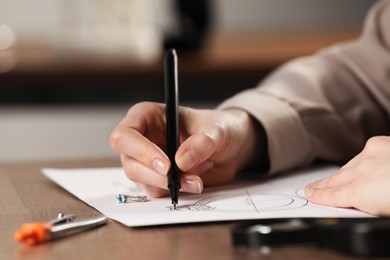 Jeweler drawing sketch of elegant ring on paper at wooden table indoors, closeup Photo of Jeweler drawing sketch of elegant ring on paper at wooden table indoors, closeup