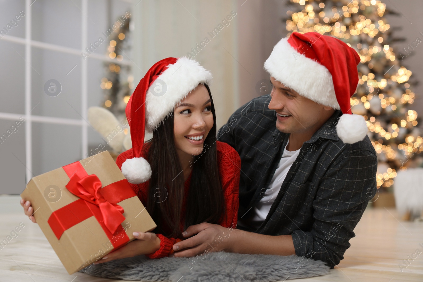 Happy young couple in Santa hats with Christmas gift at home Photo of Happy young couple in Santa hats with Christmas gift at home