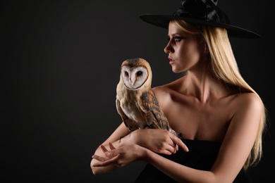 Witch in black hat with owl on dark background. Scary fantasy character Photo of Witch in black hat with owl on dark background. Scary fantasy character