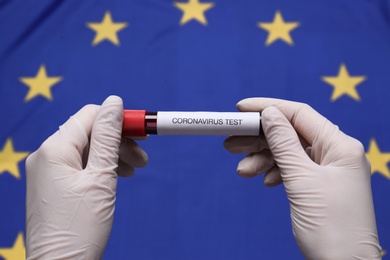 Doctor holding sample tube with label Coronavirus Test above European Union flag, closeup Photo of Doctor holding sample tube with label Coronavirus Test above European Union flag, closeup