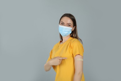 Vaccinated woman with protective mask showing medical plaster on her arm against grey background Photo of Vaccinated woman with protective mask showing medical plaster on her arm against grey background