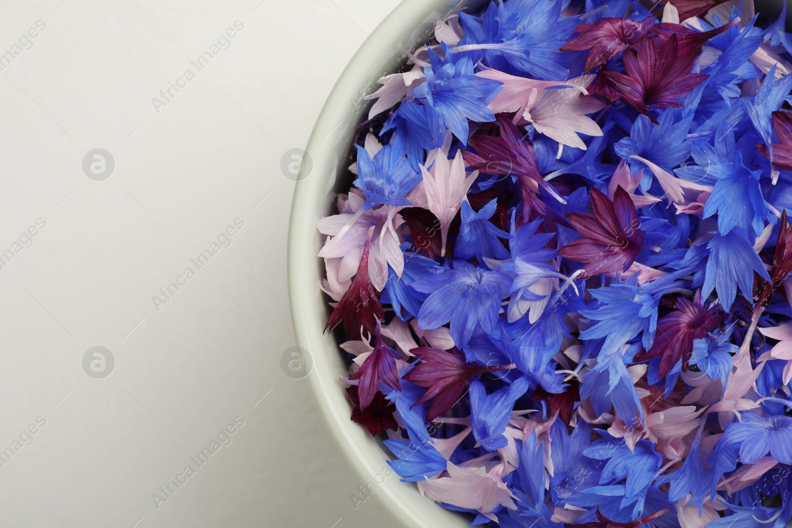 Beautiful colorful cornflowers petals in bowl on white table, top view. Space for text Photo of Beautiful colorful cornflowers petals in bowl on white table, top view. Space for text
