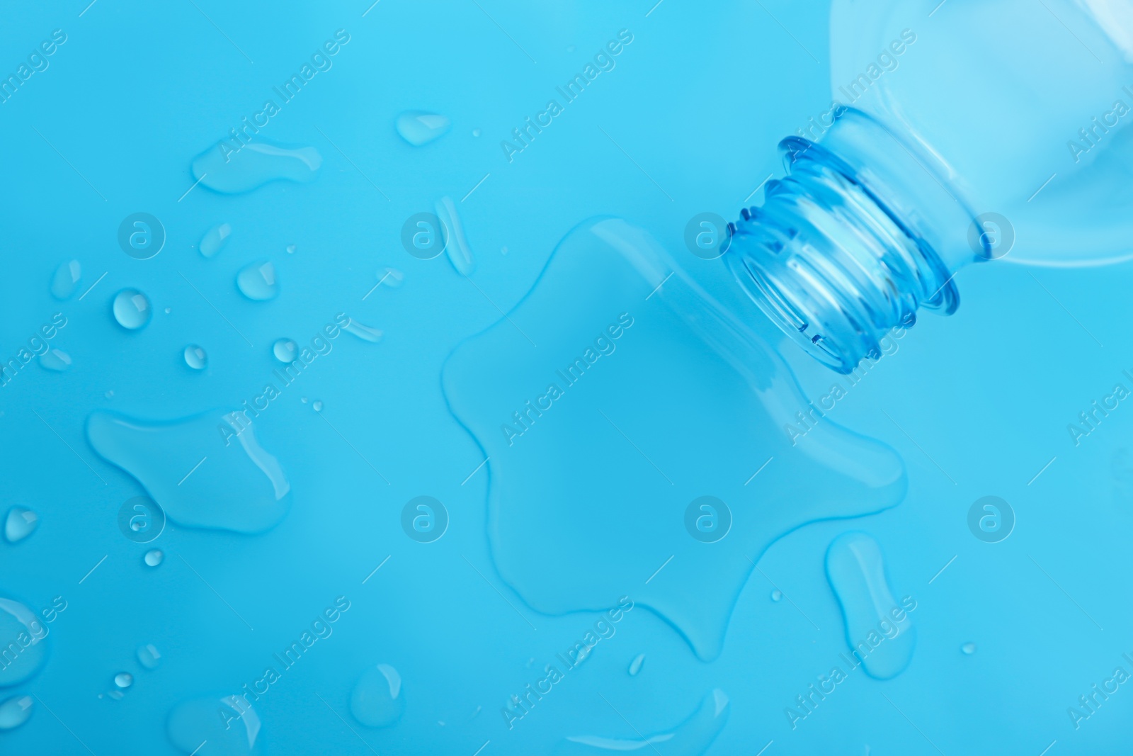 Drops of spilled water and plastic bottle on light blue background, top view Photo of Drops of spilled water and plastic bottle on light blue background, top view
