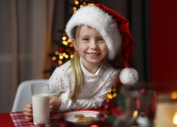 Cute little child with milk and cookies at table in dining room. Christmas time Photo of Cute little child with milk and cookies at table in dining room. Christmas time