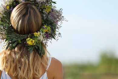 Young woman wearing wreath made of beautiful flowers outdoors on sunny day, back view Photo of Young woman wearing wreath made of beautiful flowers outdoors on sunny day, back view