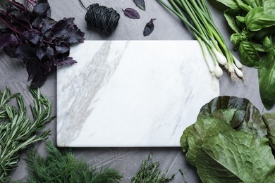Different herbs and marble cutting board on grey table, flat lay. Space for text Photo of Different herbs and marble cutting board on grey table, flat lay. Space for text