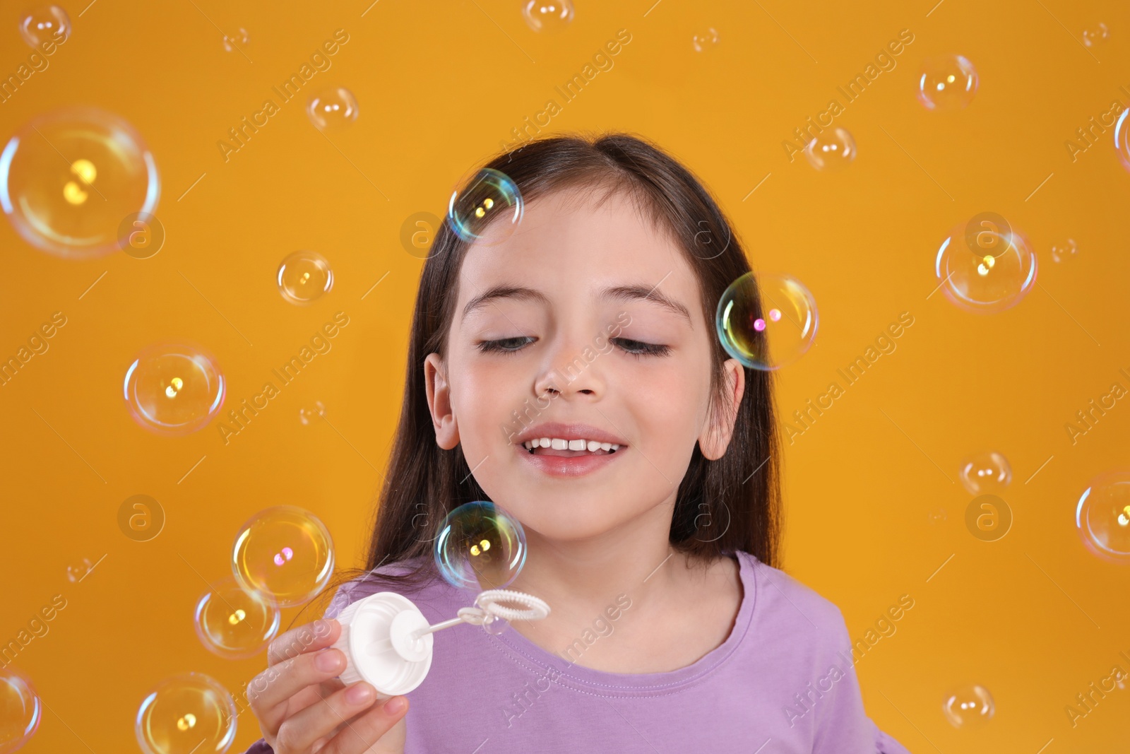 Little girl having fun with soap bubbles on yellow background Photo of Little girl having fun with soap bubbles on yellow background