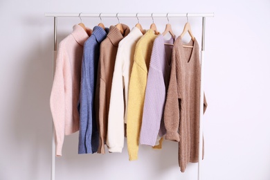 Warm sweaters hanging on rack against white background Photo of Warm sweaters hanging on rack against white background