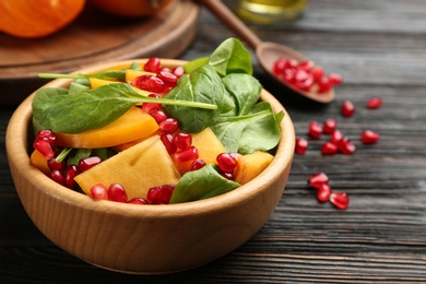 Delicious persimmon salad with pomegranate and spinach on wooden table Photo of Delicious persimmon salad with pomegranate and spinach on wooden table