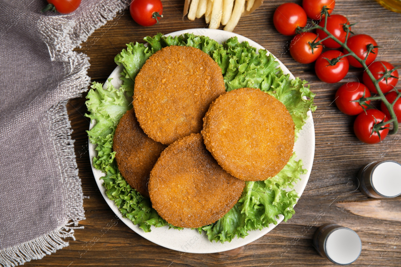Delicious fried breaded cutlets, spices and cherry tomatoes on wooden table, flat lay Photo of Delicious fried breaded cutlets, spices and cherry tomatoes on wooden table, flat lay
