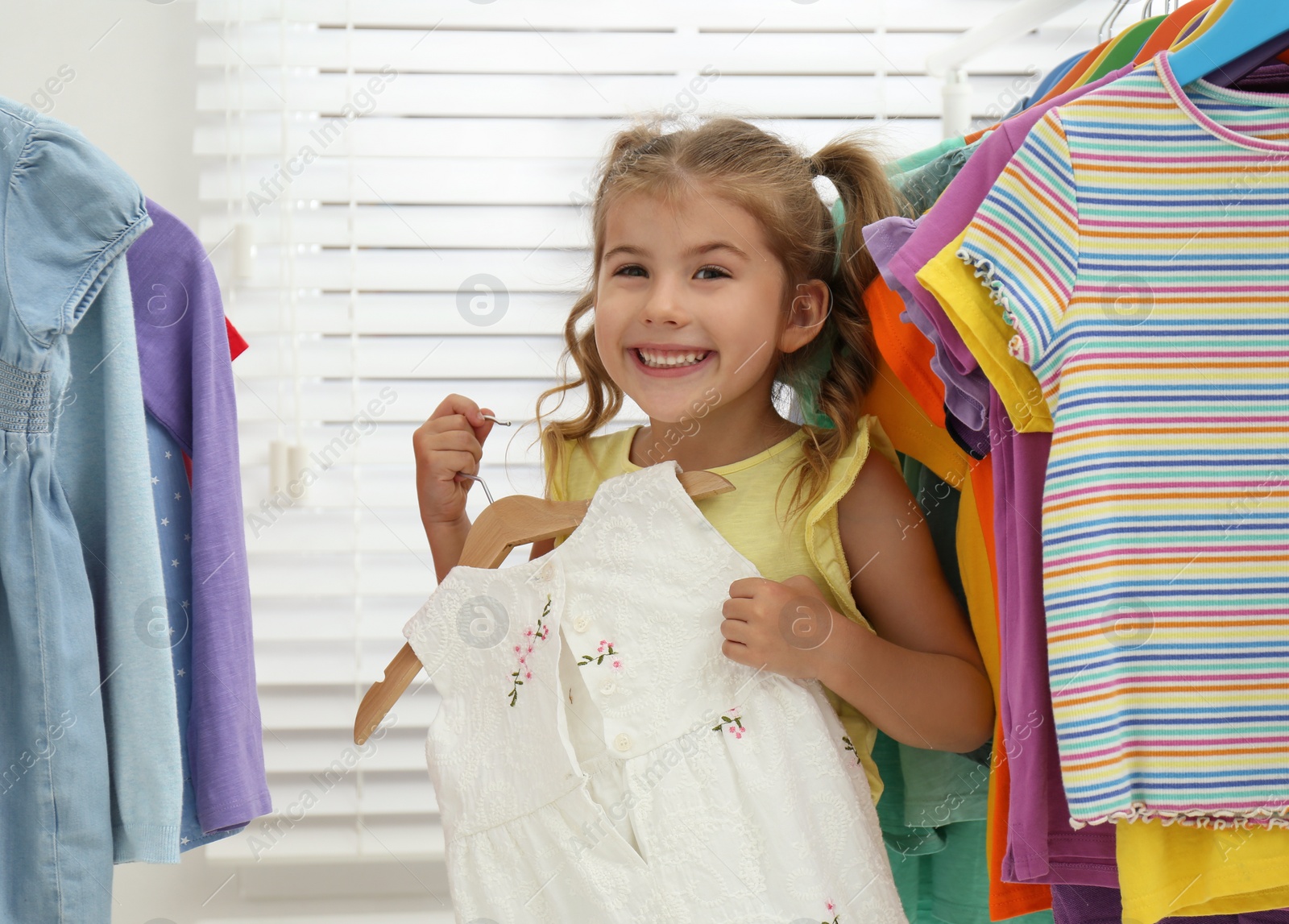 Little girl choosing clothes on rack indoors Photo of Little girl choosing clothes on rack indoors