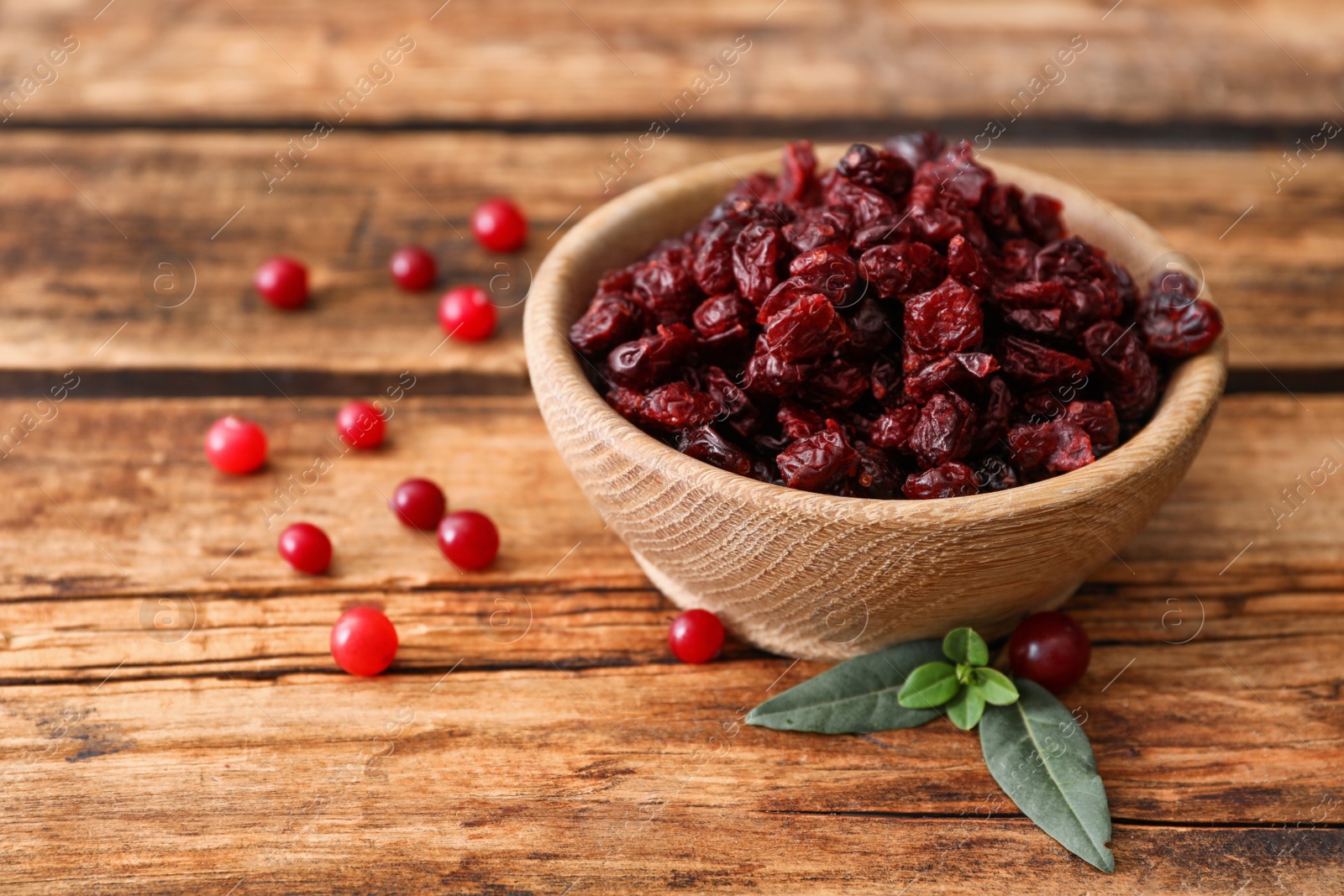 Tasty fresh and dried cranberries with leaves on wooden table Photo of Tasty fresh and dried cranberries with leaves on wooden table