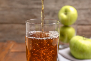 Pouring fresh apple juice into glass on wooden background, closeup Photo of Pouring fresh apple juice into glass on wooden background, closeup