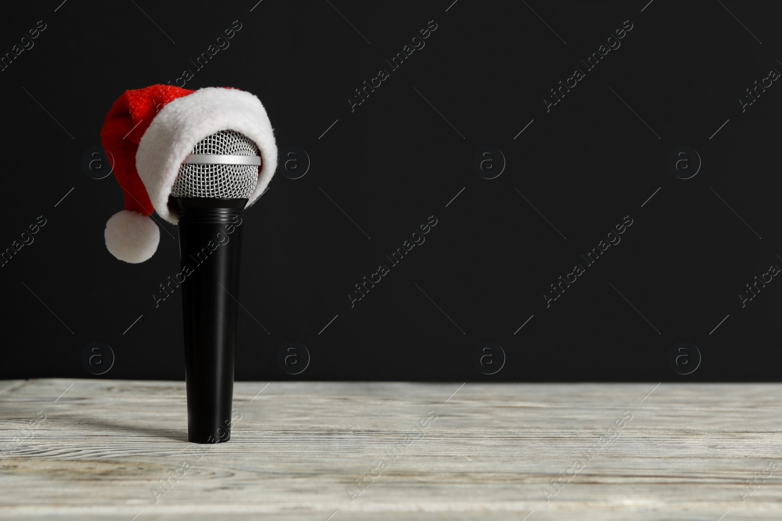 Microphone with Santa hat on white table against black background, space for text. Christmas music Photo of Microphone with Santa hat on white table against black background, space for text. Christmas music