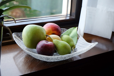 Juicy ripe fruits in vase on wooden window sill Photo of Juicy ripe fruits in vase on wooden window sill
