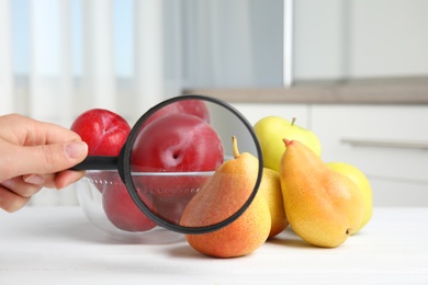 Woman with magnifying glass exploring fruits indoors, closeup. Poison detection Photo of Woman with magnifying glass exploring fruits indoors, closeup. Poison detection