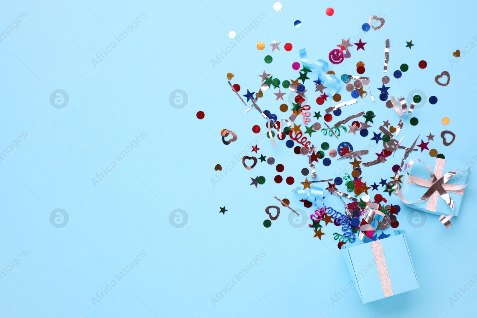Colorful confetti and box on light blue background, top view. Space for text Photo of Colorful confetti and box on light blue background, top view. Space for text