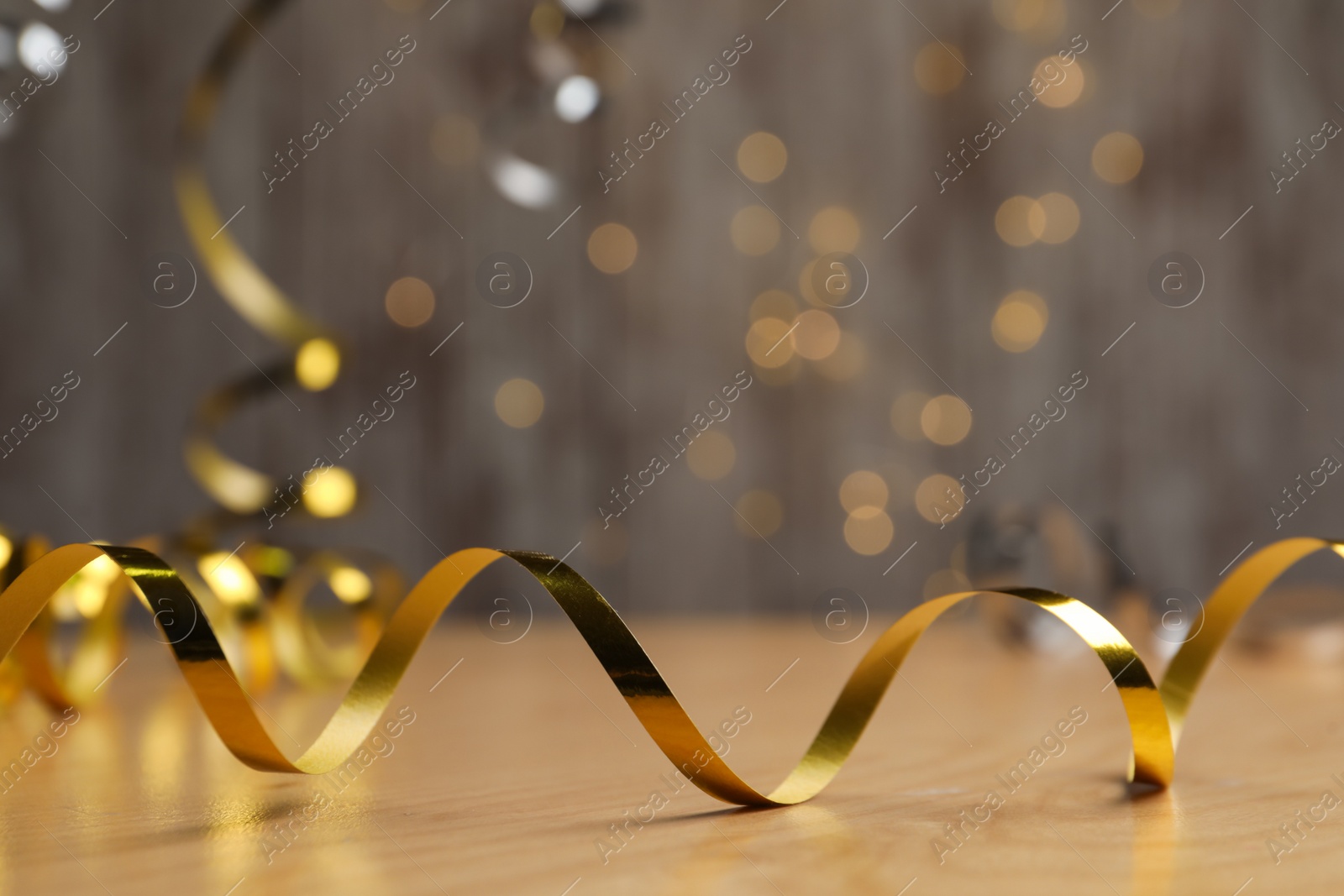 Shiny golden serpentine streamer on wooden table against blurred lights. Space for text Photo of Shiny golden serpentine streamer on wooden table against blurred lights. Space for text