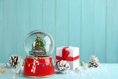 Beautiful snow globe, gift box and Christmas decor on light blue table, space for text Photo of Beautiful snow globe, gift box and Christmas decor on light blue table, space for text