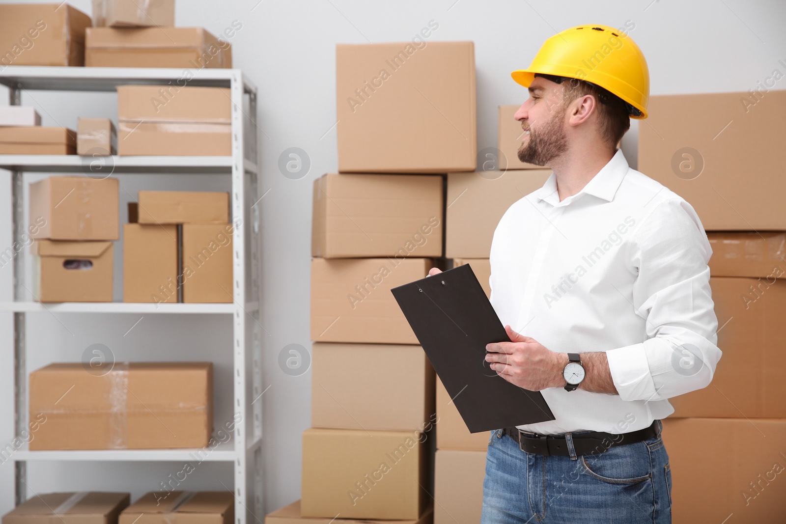 Young man with clipboard near cardboard boxes at warehouse Photo of Young man with clipboard near cardboard boxes at warehouse