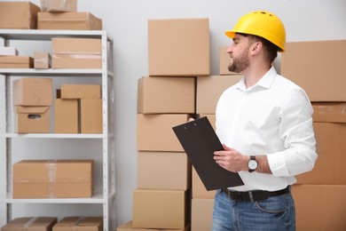 Young man with clipboard near cardboard boxes at warehouse Photo of Young man with clipboard near cardboard boxes at warehouse
