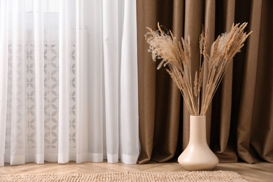Fluffy reed plumes near window indoors, space for text. Interior element Photo of Fluffy reed plumes near window indoors, space for text. Interior element