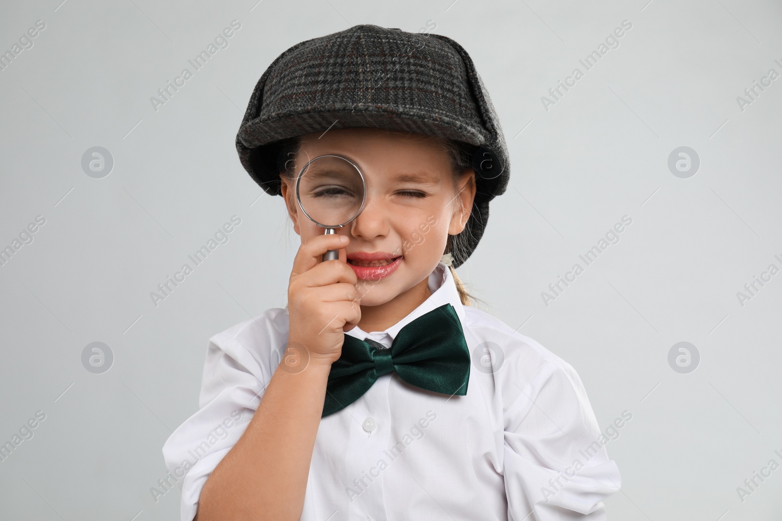 Cute little detective with magnifying glass on grey background Photo of Cute little detective with magnifying glass on grey background