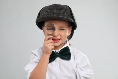 Cute little detective with magnifying glass on grey background Photo of Cute little detective with magnifying glass on grey background