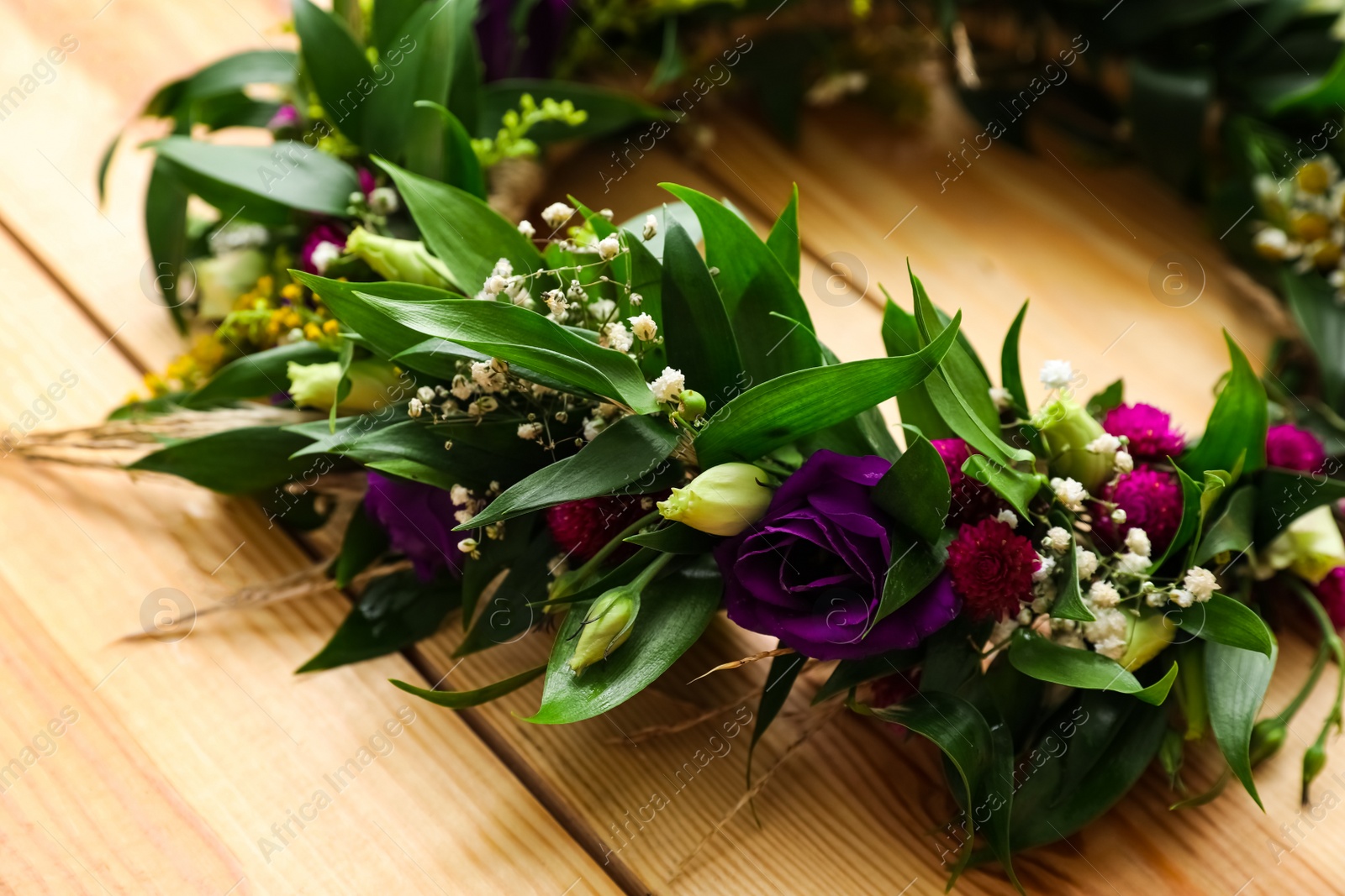 Photo of Beautiful wreath made of flowers and leaves on wooden background, closeup