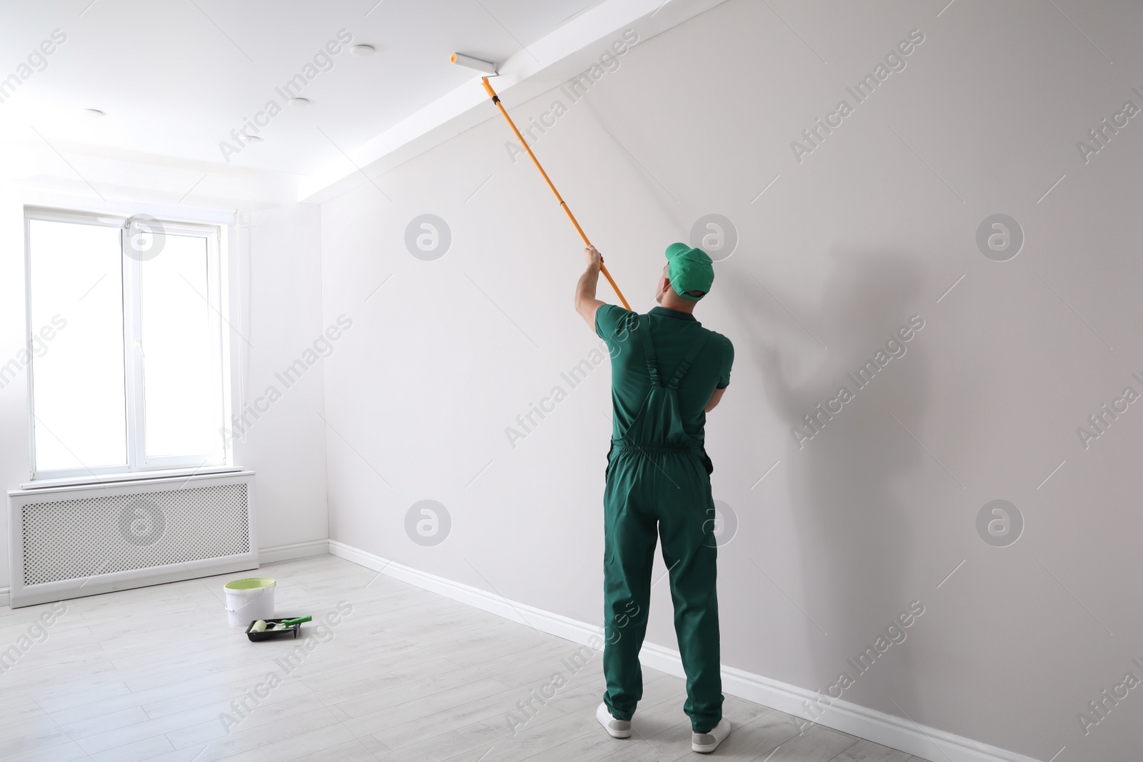 Man painting ceiling with roller in room, back view Photo of Man painting ceiling with roller in room, back view