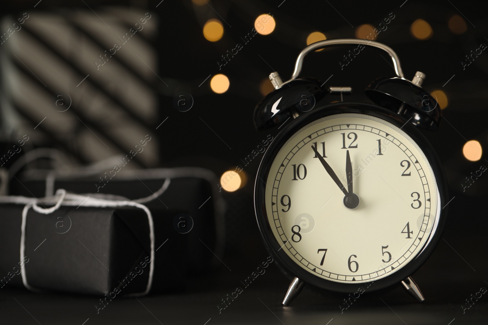 Vintage alarm clock with decor on black table against blurred Christmas lights, closeup. New Year countdown Photo of Vintage alarm clock with decor on black table against blurred Christmas lights, closeup. New Year countdown