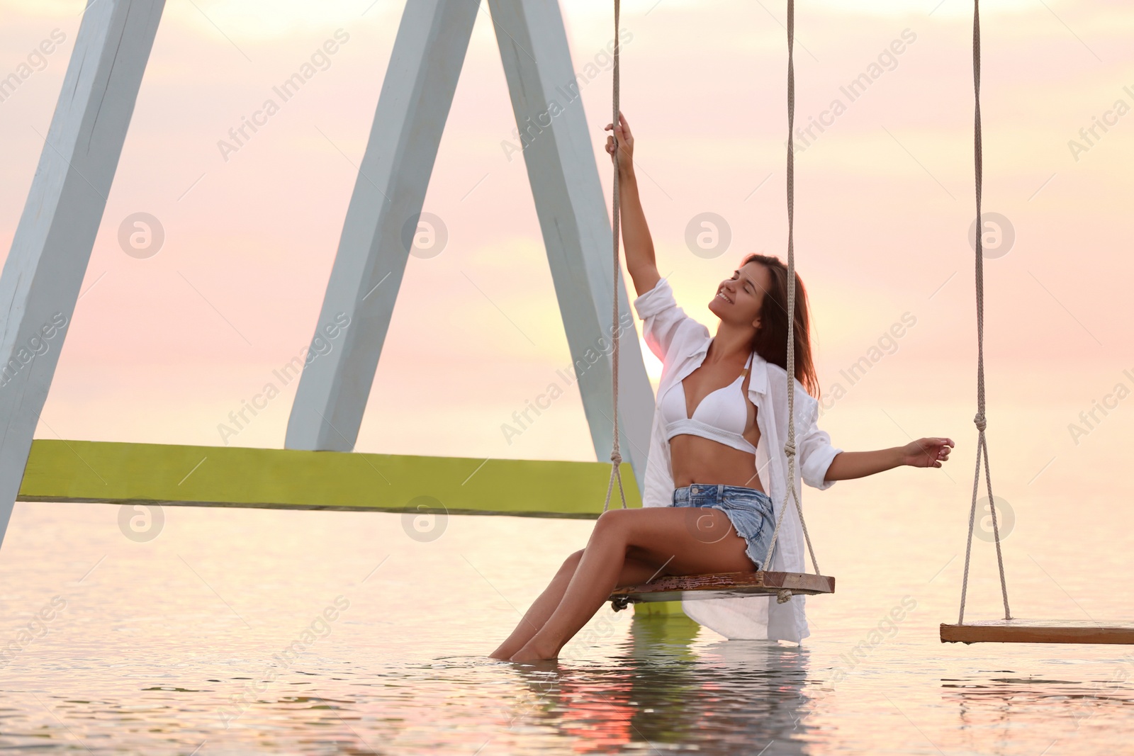 Young woman enjoying sunrise on swing over water Photo of Young woman enjoying sunrise on swing over water