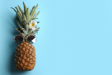 Top view of funny pineapple with sunglasses and plumeria flower on light blue background, space for text. Creative concept Photo of Top view of funny pineapple with sunglasses and plumeria flower on light blue background, space for text. Creative concept