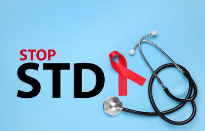 Red awareness ribbon, stethoscope and text Stop STD on light blue background, flat lay Image of Red awareness ribbon, stethoscope and text Stop STD on light blue background, flat lay