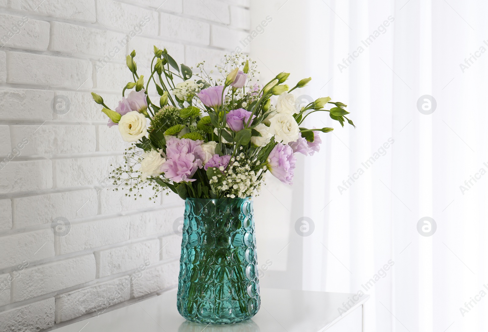 Bouquet of beautiful Eustoma flowers on table near white brick wall Photo of Bouquet of beautiful Eustoma flowers on table near white brick wall