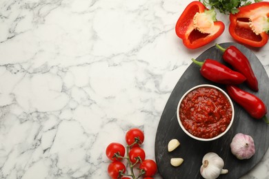 Delicious adjika sauce in bowl and ingredients on white marble table, flat lay. Space for text Photo of Delicious adjika sauce in bowl and ingredients on white marble table, flat lay. Space for text