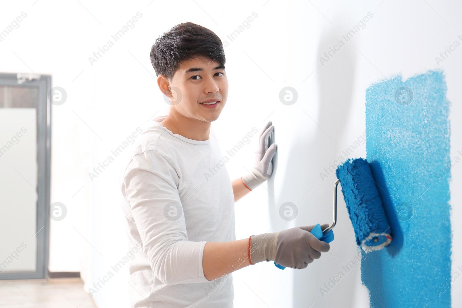 Male decorator painting wall with roller indoors Photo of Male decorator painting wall with roller indoors