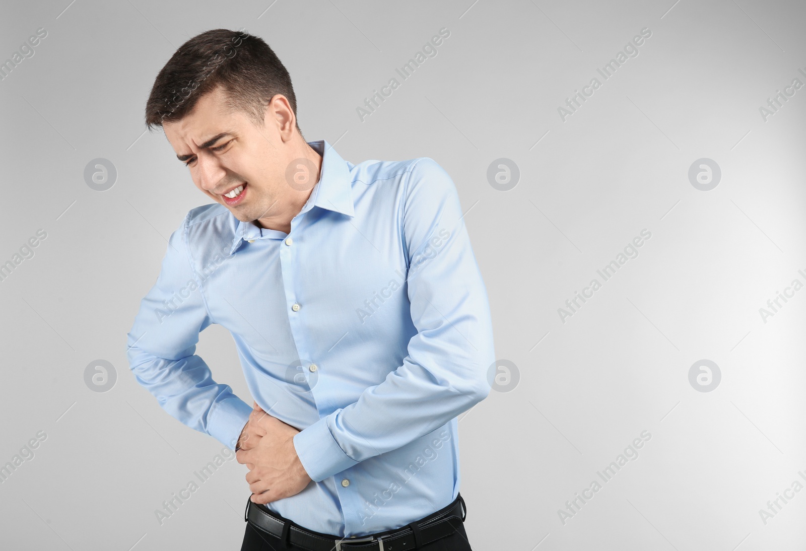 Young man suffering from flank pain on light background Photo of Young man suffering from flank pain on light background